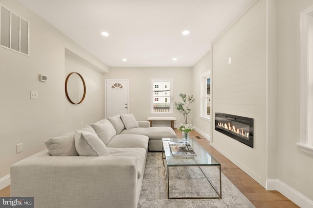 living area with a glass covered fireplace, wood finished floors, visible vents, and baseboards