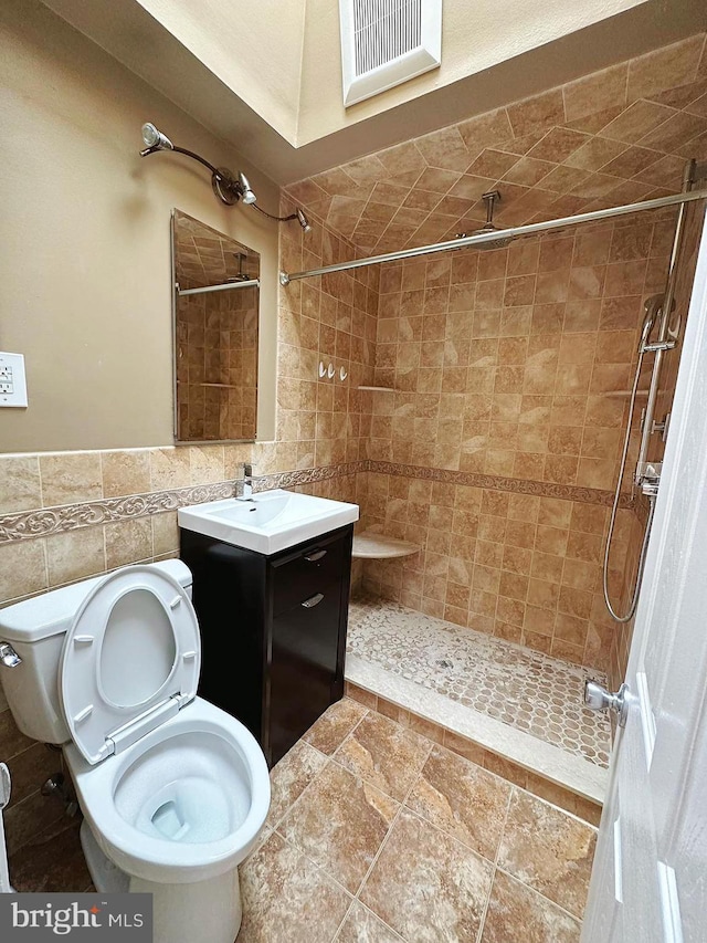 bathroom featuring vanity, a tile shower, tile walls, and toilet