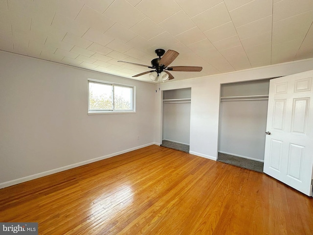 unfurnished bedroom featuring hardwood / wood-style floors, two closets, and ceiling fan