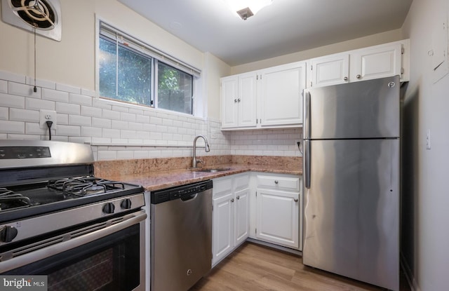 kitchen with sink, light stone counters, light hardwood / wood-style flooring, appliances with stainless steel finishes, and white cabinets