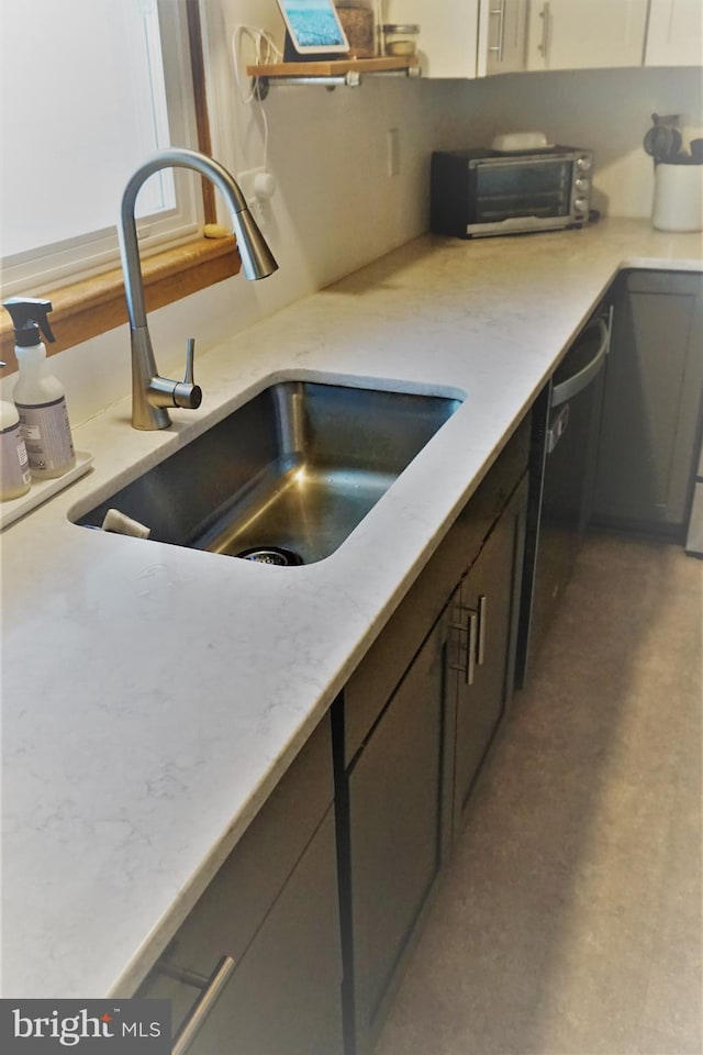 kitchen with light stone counters, sink, gray cabinetry, and dishwasher