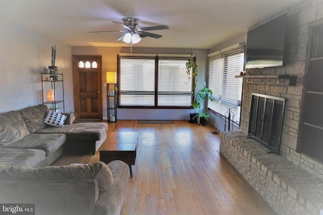 living room featuring ceiling fan, wood-type flooring, and a brick fireplace