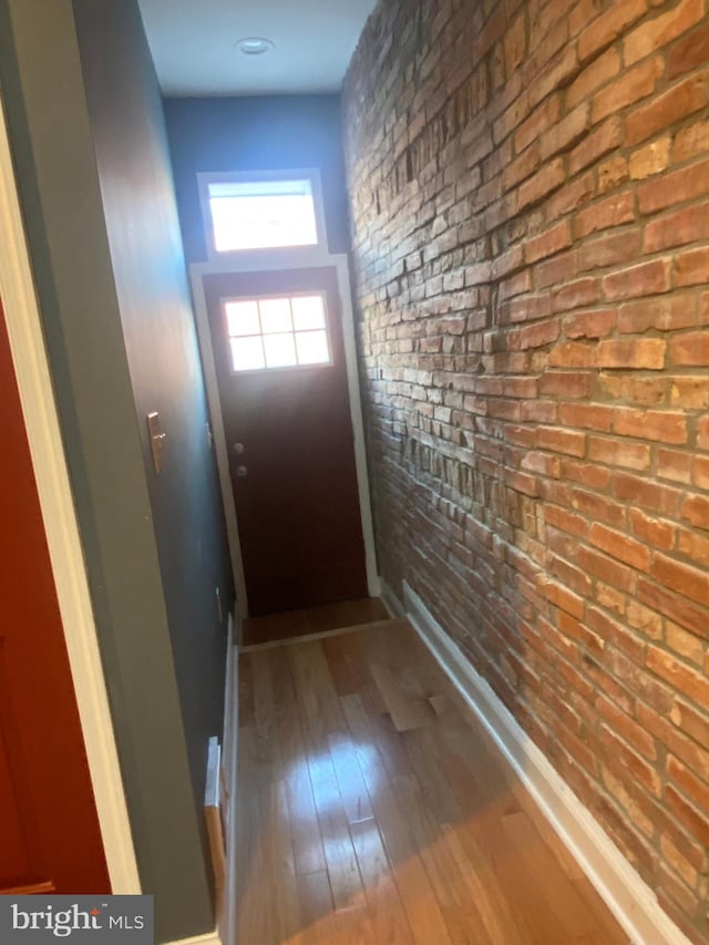 doorway to outside featuring hardwood / wood-style flooring and brick wall