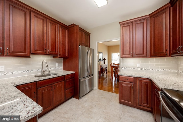 kitchen featuring sink, stainless steel appliances, tasteful backsplash, and light stone countertops