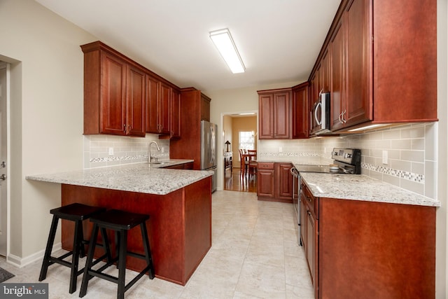 kitchen with stainless steel appliances, a breakfast bar, sink, backsplash, and light stone counters