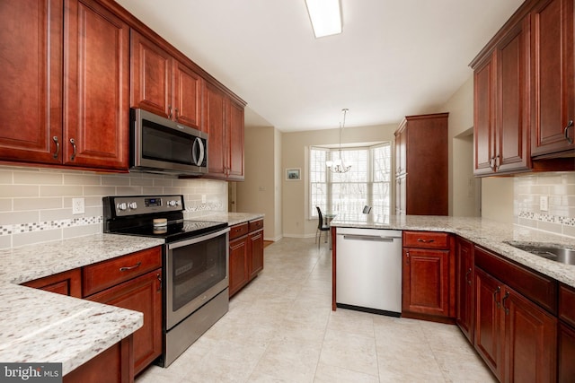 kitchen with kitchen peninsula, hanging light fixtures, light stone countertops, a notable chandelier, and appliances with stainless steel finishes