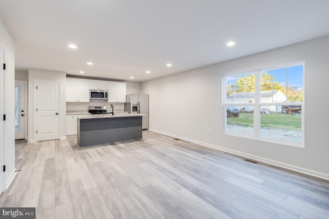 kitchen featuring white cabinetry, light wood-type flooring, stainless steel appliances, light stone countertops, and a kitchen island with sink