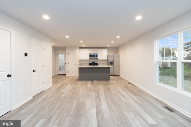 kitchen with white cabinetry, a center island with sink, light hardwood / wood-style floors, and appliances with stainless steel finishes