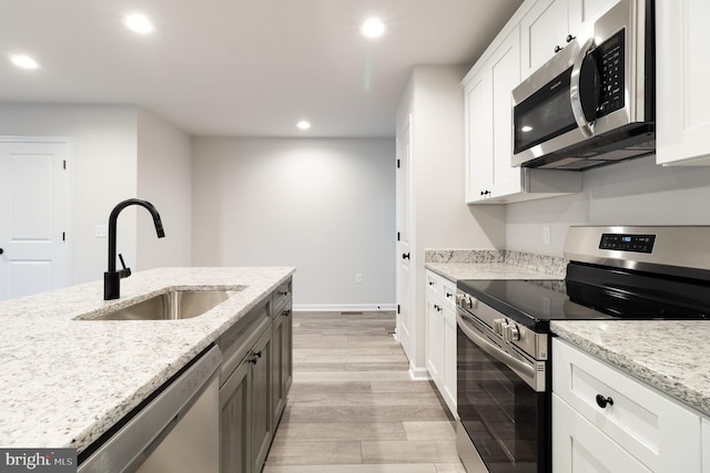 kitchen with sink, light wood-type flooring, appliances with stainless steel finishes, light stone countertops, and white cabinets