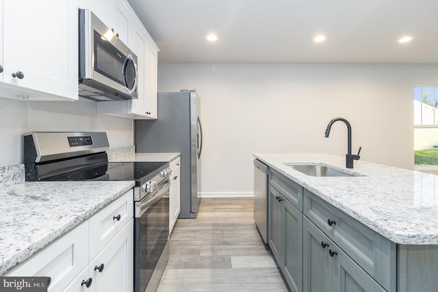 kitchen with appliances with stainless steel finishes, sink, white cabinets, light stone countertops, and light wood-type flooring