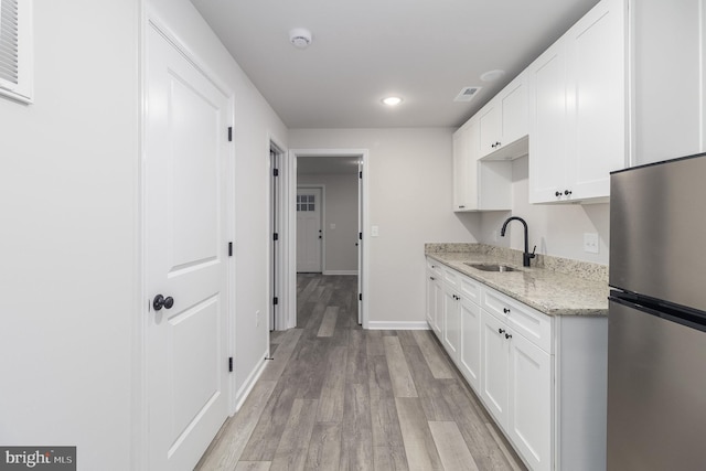 kitchen featuring stainless steel refrigerator, sink, light stone counters, and white cabinets