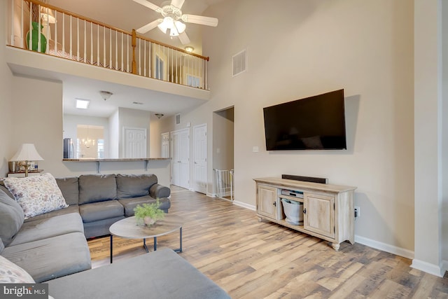 living room with ceiling fan with notable chandelier, a towering ceiling, and light hardwood / wood-style floors