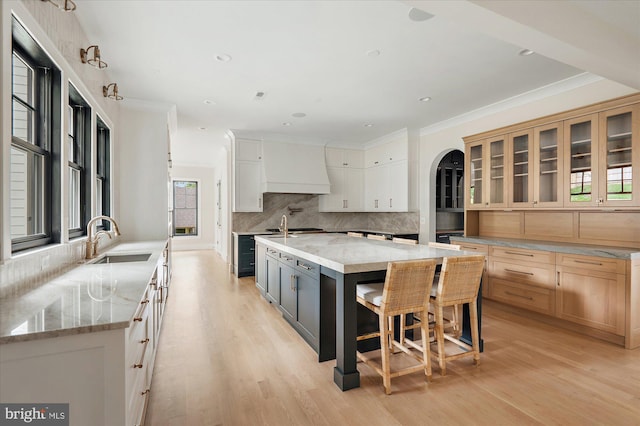 kitchen with custom exhaust hood, a spacious island, glass insert cabinets, white cabinetry, and a sink