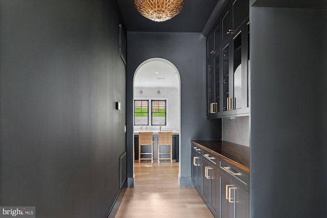 bar with light wood-style flooring, visible vents, arched walkways, and tasteful backsplash