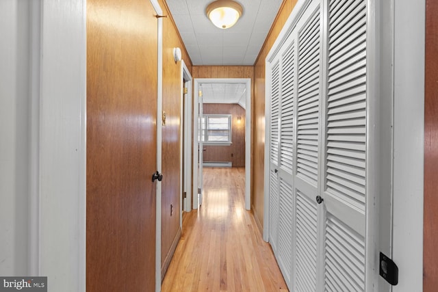 hall with baseboard heating, wooden walls, and light wood-type flooring