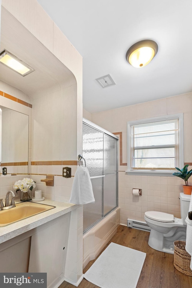 full bathroom featuring toilet, sink, tile walls, a baseboard radiator, and hardwood / wood-style flooring