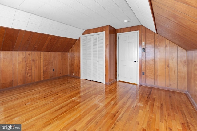 bonus room with lofted ceiling, wooden walls, and light hardwood / wood-style flooring