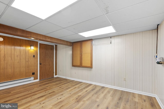 basement featuring a paneled ceiling, light hardwood / wood-style floors, and baseboard heating