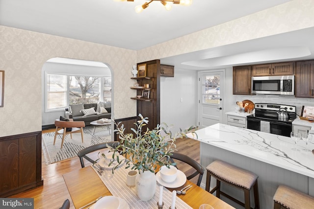 kitchen featuring appliances with stainless steel finishes, a breakfast bar area, kitchen peninsula, dark brown cabinets, and light wood-type flooring