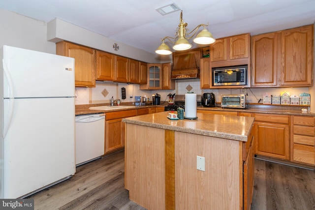 kitchen featuring glass insert cabinets, a kitchen island, a sink, white appliances, and premium range hood