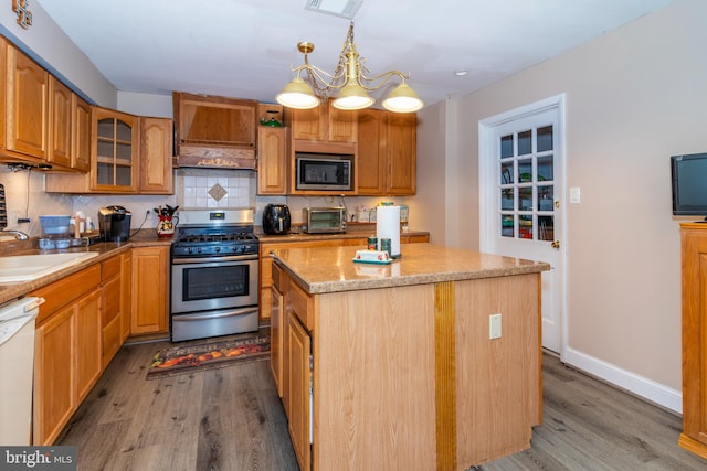 kitchen featuring stainless steel appliances, premium range hood, a sink, a center island, and glass insert cabinets