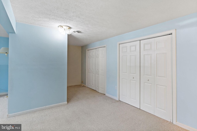 unfurnished bedroom with two closets, light colored carpet, and a textured ceiling