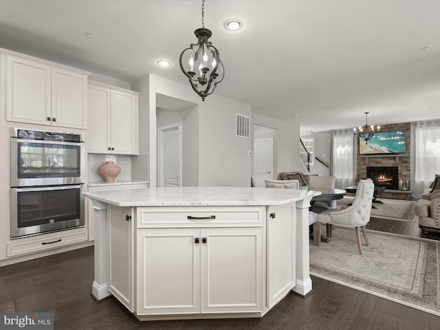 kitchen featuring white cabinetry, hanging light fixtures, a kitchen island, a notable chandelier, and stainless steel double oven