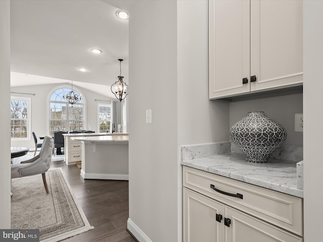 interior space with pendant lighting, dark wood-type flooring, white cabinetry, light stone countertops, and a chandelier