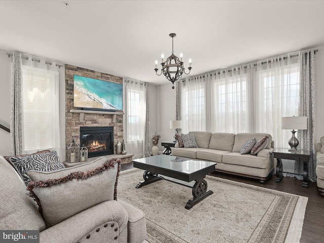 living room featuring a stone fireplace, a healthy amount of sunlight, a chandelier, and dark hardwood / wood-style floors