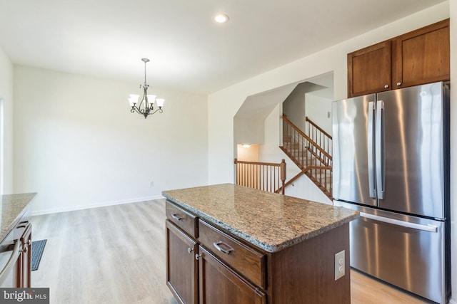 kitchen featuring a kitchen island, stainless steel refrigerator, dark stone countertops, hanging light fixtures, and light wood-type flooring