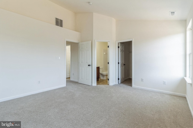 unfurnished bedroom featuring light carpet, ensuite bath, high vaulted ceiling, and a spacious closet