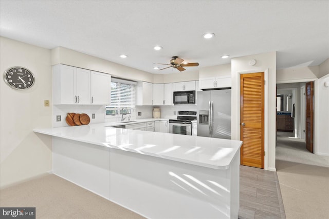 kitchen featuring light countertops, appliances with stainless steel finishes, white cabinetry, a sink, and a peninsula