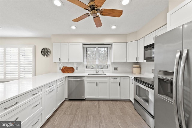 kitchen with stainless steel appliances, light countertops, a sink, and white cabinetry