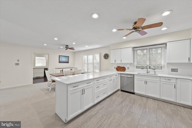 kitchen with dishwasher, a peninsula, light countertops, white cabinetry, and a sink