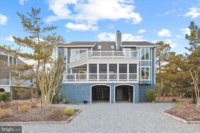 raised beach house with a carport, a sunroom, a chimney, and gravel driveway