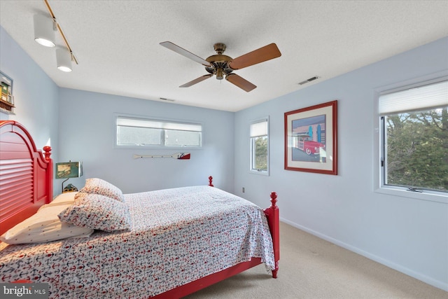 carpeted bedroom featuring baseboards, visible vents, ceiling fan, and a textured ceiling