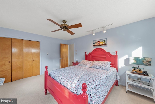 bedroom with rail lighting, a closet, light colored carpet, and ceiling fan