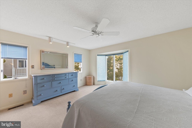 bedroom with light colored carpet, visible vents, a textured ceiling, and rail lighting