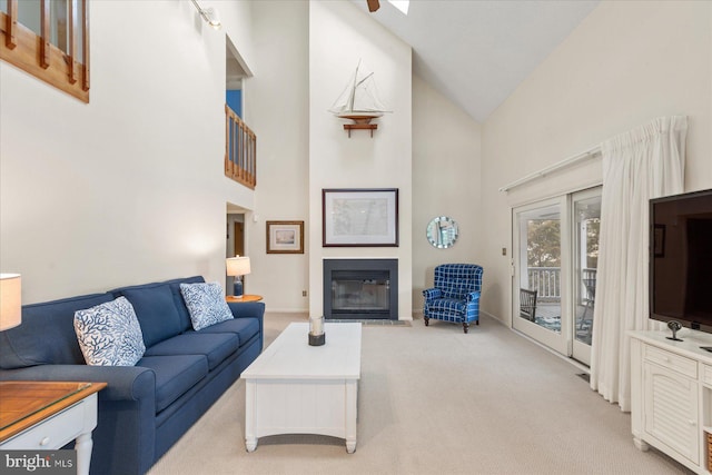 living area featuring high vaulted ceiling, a glass covered fireplace, and light colored carpet