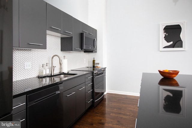 kitchen with appliances with stainless steel finishes, sink, dark hardwood / wood-style flooring, dark stone counters, and decorative backsplash