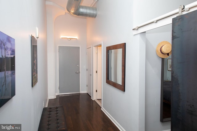 hallway with dark wood-type flooring, a towering ceiling, and a barn door