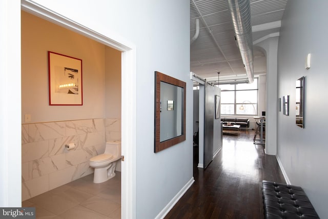 hall featuring dark wood-type flooring, a barn door, and tile walls