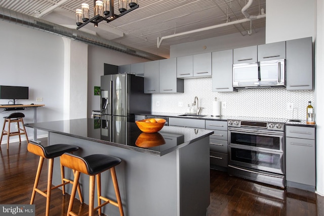 kitchen with dark wood-type flooring, sink, tasteful backsplash, appliances with stainless steel finishes, and a kitchen breakfast bar