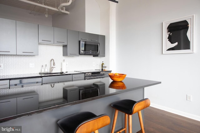 kitchen with sink, dark wood-type flooring, backsplash, stainless steel appliances, and a kitchen bar