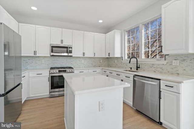 kitchen with appliances with stainless steel finishes, sink, light wood-type flooring, a kitchen island, and white cabinets