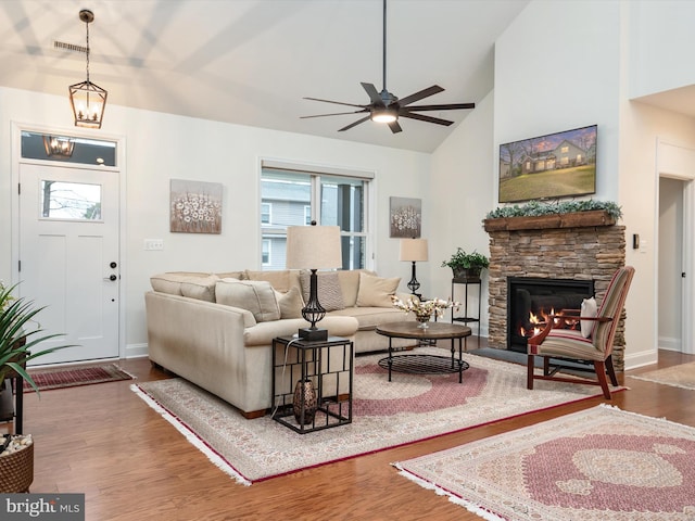 living room with dark hardwood / wood-style flooring, ceiling fan, a stone fireplace, and a healthy amount of sunlight