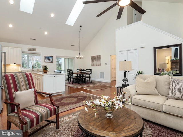 living room featuring wood-type flooring, ceiling fan with notable chandelier, high vaulted ceiling, and a skylight