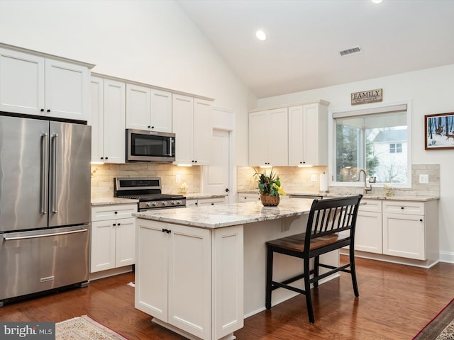 kitchen with appliances with stainless steel finishes, dark hardwood / wood-style flooring, a kitchen island, light stone countertops, and white cabinets