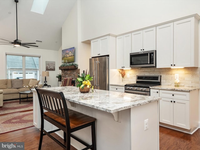 kitchen with white cabinetry, a kitchen bar, light stone counters, and appliances with stainless steel finishes