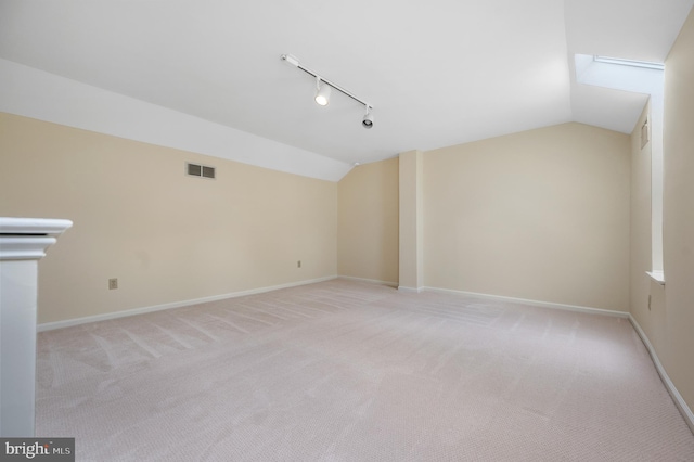 spare room featuring lofted ceiling, light carpet, and rail lighting